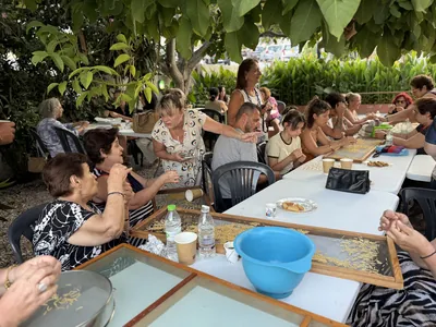 Participants making traditional pasta by hand at outdoor tables under the trees.